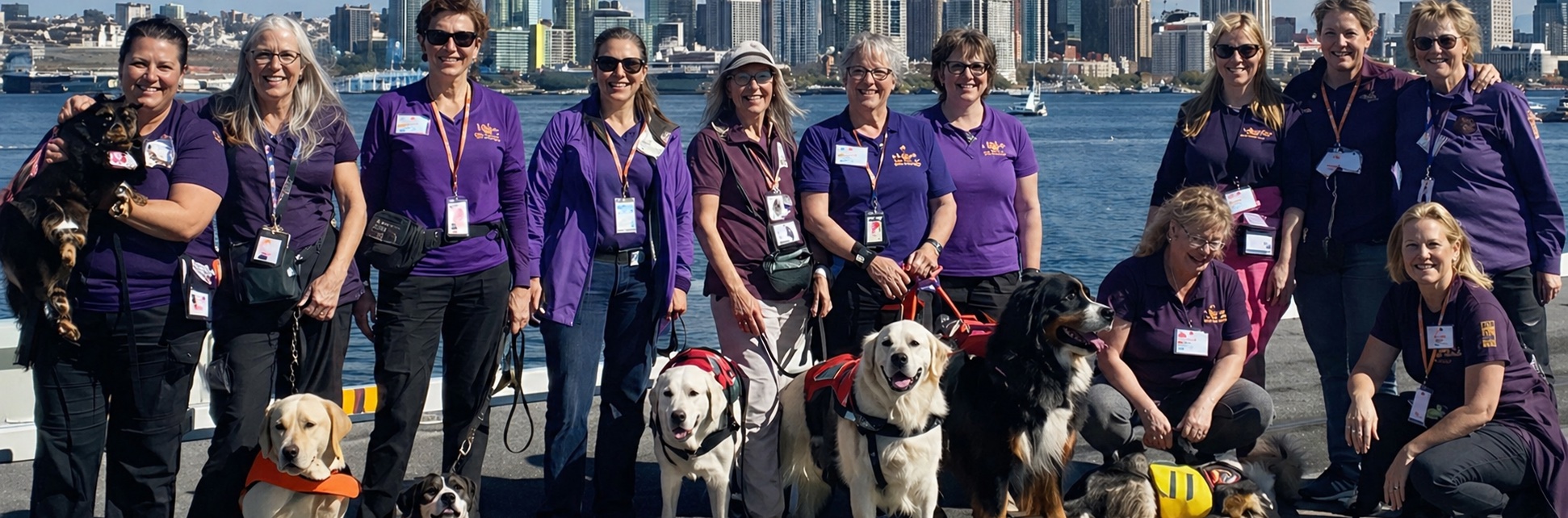 A large group of National Crisis Response Canine teams posing on a ferry dock with a city skyline in the background.