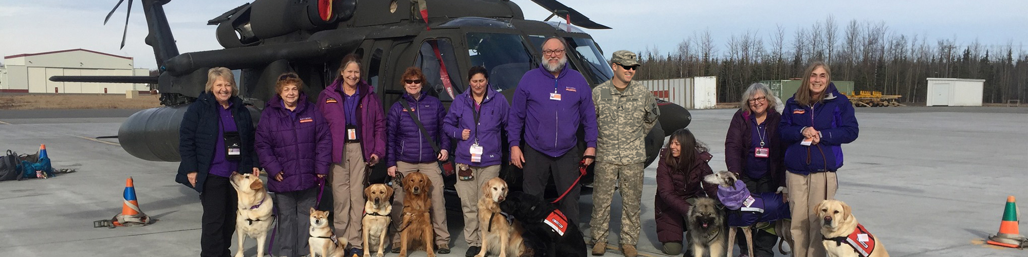 National Crisis Response Canine teams - dogs and their handlers - pose in front of a military helicopter.