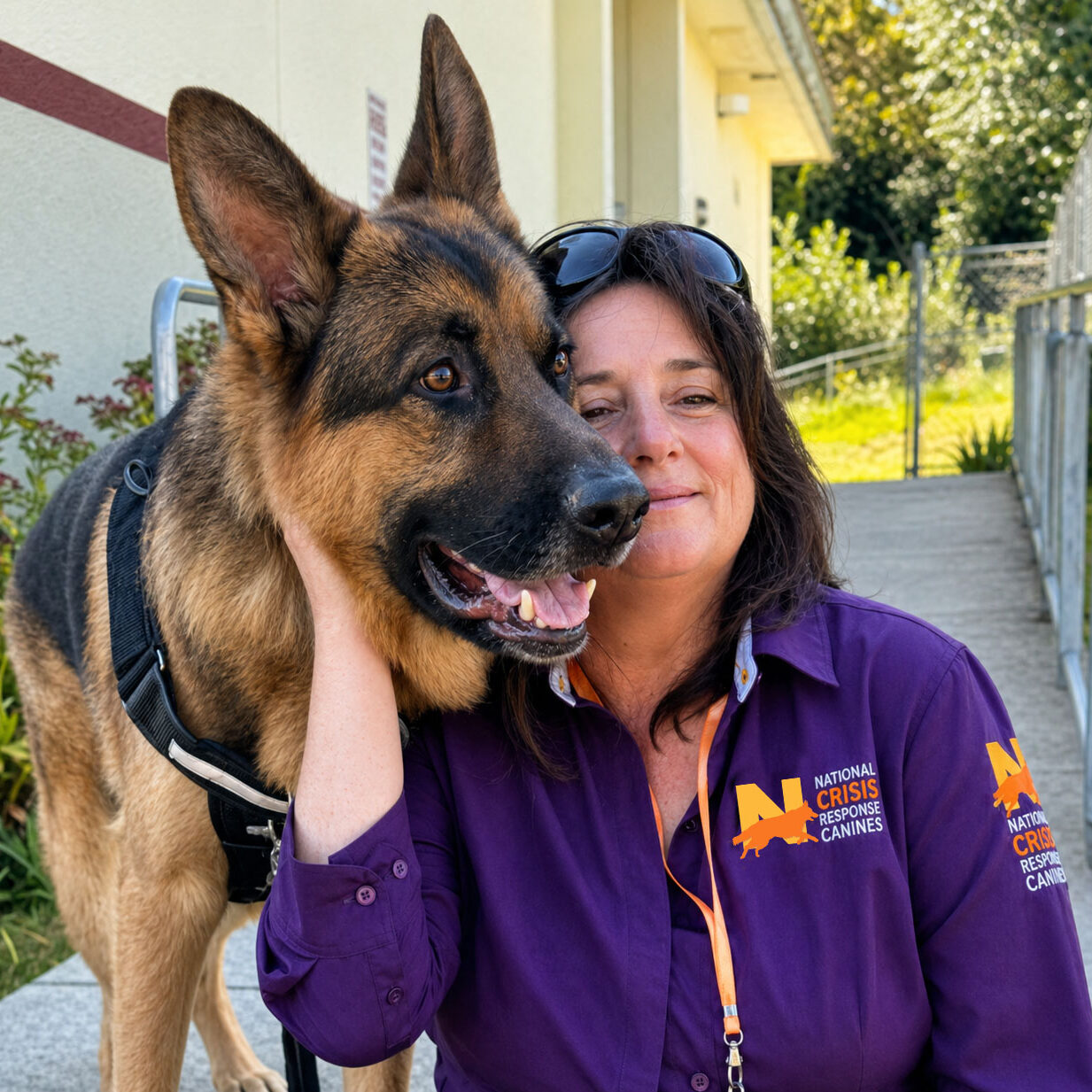 German Shepherd cheek to cheek with its handler wearing a National Crisis Response Canines uniform.